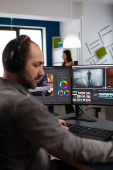 maker with headset working with footage and sound on pc with two displays, taking notes while editing customer creative . Man editor processing film montage in startup agency office. photo