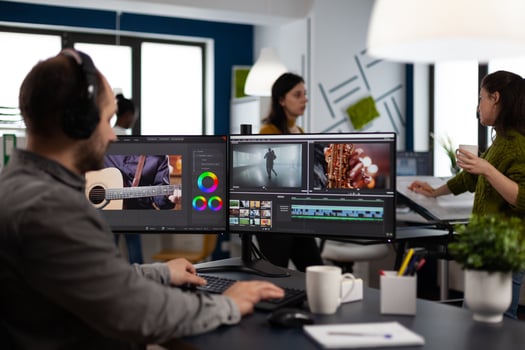 Videographer listening music on headphones editing creative movie using post production software working in business multimedia agency office. Artist man processing audio film montage on computer photo