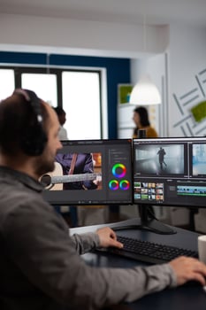 Videographer listening music on headphones editing creative movie using post production software working in business multimedia agency office. Artist man processing audio film montage on computer photo