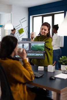 Women videographers editing project creating multimedia content, team of bloggers working in modern creativity office studio. Manager explaning to colleaque film montage discussing production photo
