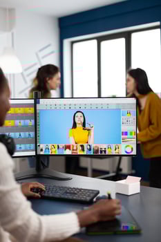 Black retoucher artist analysing images on pc with two monitors and retouching digital assets with stylus pencil. African designer using photo editing software working in creative production office