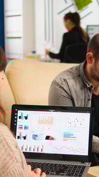 Close up of back view young entrepreneur sitting on couch in office using laptop computer while colleagues working on background. Multiethnic coworkers planning new financial project in modern company photo
