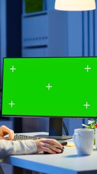Woman looking at computer with chroma key during night time in start up business office working overtime. Freelancer watching desktop monitor mockup display with green screen, typing writting photo