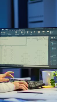 Woman architect matching digital plans from pc with blueprints working in start-up business office overtime. Designer using cad software to design a 3D concept of buildings creating late at night photo