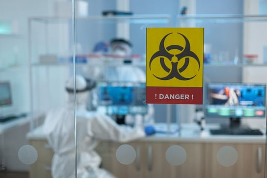 Selective focus on danger sign in microbiological hospital laboratory during chemical experiment. Teamwork of scientist with coronavirus protective medical equipment working at medicine vaccine photo
