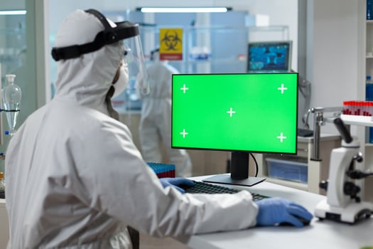 Biologist man with protection ppe medical suit looking at mock up green screen chroma key computer with isolated display while working in biochemistry hospital laboratory. Covid19 vaccine development photo