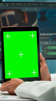 Male chemist scientist holding green mock-up screen tablet sitting at desk. In background technology research, development laboratory with specialist doctor working in high tech design photo
