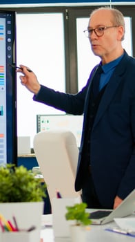Mature CEO CTO executive director presenting statistical data, financial project briefing diverse group of employees. Multiethnical team working in professional startup company during conference meeting photo
