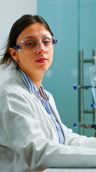 Portrait of tired scientist trying to smile at camera sitting in modern equipped laboratory typing on computer. Chemist examining virus evolution using high tech for scientific research, vaccine photo