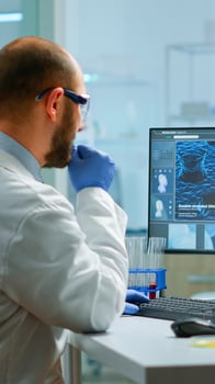 Man biologist checking DNA informations typing on pc in modern equipped laboratory. Scientists examining vaccine evolution in medical lab using high tech, chemistry tools for scientific research. photo