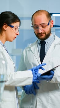 Scientist team meeting and discusssing treatment results standing in research laboratory pointing on tablet. Stuff examining vaccine development against covid19 virus using high tech for researching. photo
