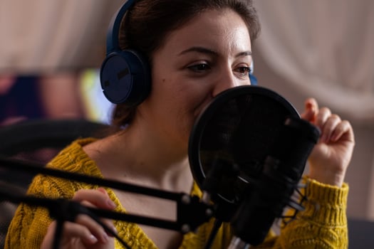 Closeup of vlogger woman with headphones talking into production microphone preparing online podcast at home in living room. Blogger influencer streaming live content answering question photo