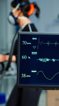 Medical researcher examining EKG image showing on monitor while patinet with mask running on cross trainer testing heart rate using electrodes.Doctor monitoring physical endurance in science sport lab photo