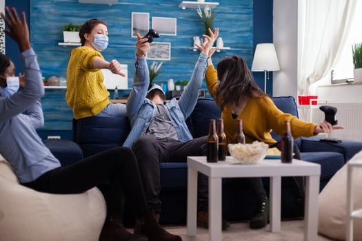 Man losing game competiton against multi ethnic friends in home living room wearing face mask keeping social distancing as prevention during covid outbreak. New normal party. photo