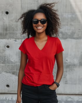 A woman in a red v-neck t-shirt stands confidently against a concrete wall photo