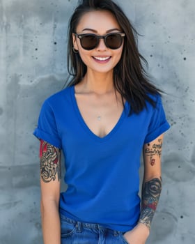 A woman in a blue v-neck t-shirt stands against a concrete wall, smiling and looking directly at the camera photo
