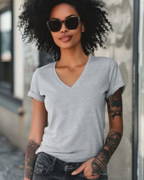 A woman wearing a gray V-neck T-shirt and sunglasses stands confidently on a city street photo