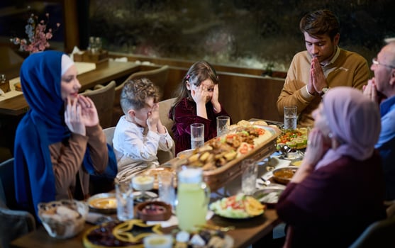 In a modern restaurant setting, a European Islamic family comes together for iftar during Ramadan, engaging in prayer before the meal, uniting tradition and contemporary practices in a celebration of photo
