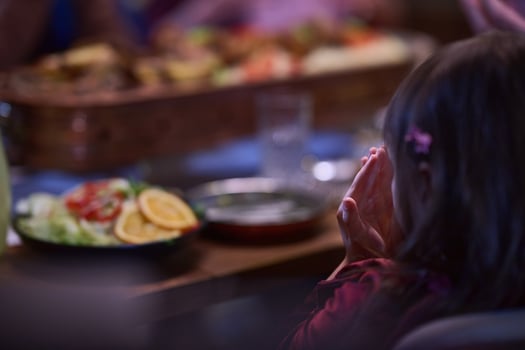A young girl raises her hands in prayer as she prepares for her iftar meal during the holy month of Ramadan, embodying spiritual devotion and innocence. photo