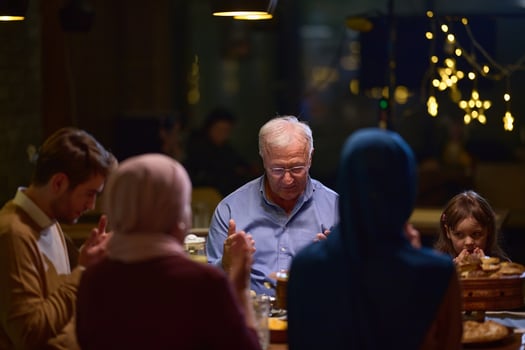 In a modern restaurant setting, a European Islamic family comes together for iftar during Ramadan, engaging in prayer before the meal, uniting tradition and contemporary practices in a celebration of photo