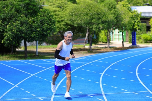 Senior Asian athlete is practicing running in the professional blue track for professional exercise, sport training workout and healthy for longevity photo