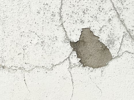 A white wall with a hole in it. The wall is cracked and has a rough texture photo