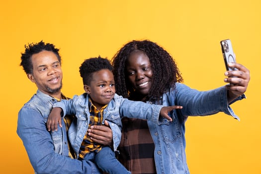 African american parents taking selfies with their small child in studio, posing together and making memories. Young mom and dad enjoying time with their boy, take pictures on phone. photo