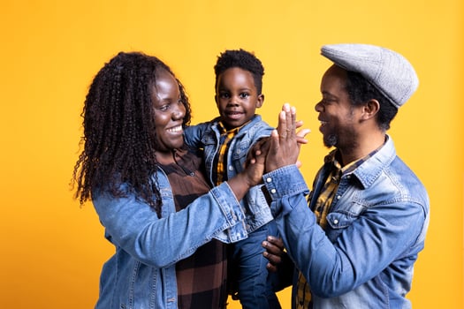 Happy black family sharing a high five together in the studio, feeling cheerful and showing affection to each other. African american couple with a small toddler posing with gratitude. photo