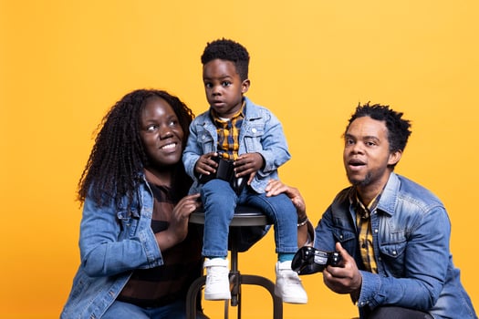 Cheerful satisfied father playing games with his toddler using a joystick, young parents having fun with their small boy. African american loving father plays with kid online. photo