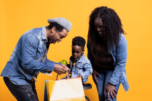Curious little boy searching shopping bags for toys in the studio, looking for fun activities while his parents and playing with him. Happy african american family of three posing on camera. photo