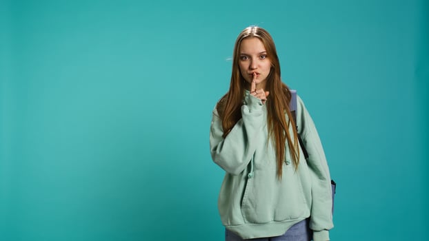 Stern woman doing shushing hand gesturing, irritated by noise, having negative mood. Girl placing finger on lips, doing quiet sign gesture, isolated over studio background, camera B photo