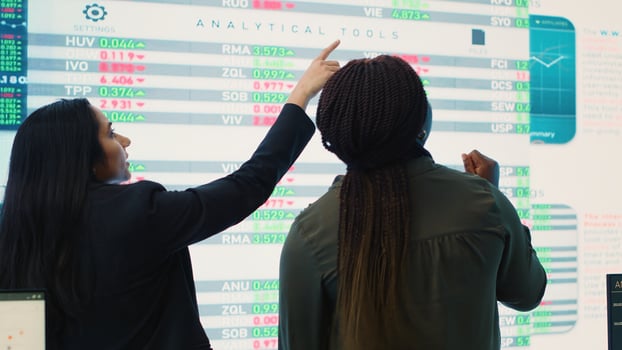 Diverse team of analysts examining monthly cost and revenue elements on a big screen, working on creating a financial projection for future improvements and success within the organization. Camera A. photo
