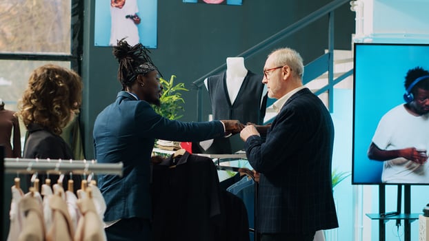 African american store assistant helping old customer to match tie with a shirt, creating an elegant outfit in fashion showroom. Employee assisting fashionable elderly client at mall. Camera A. photo