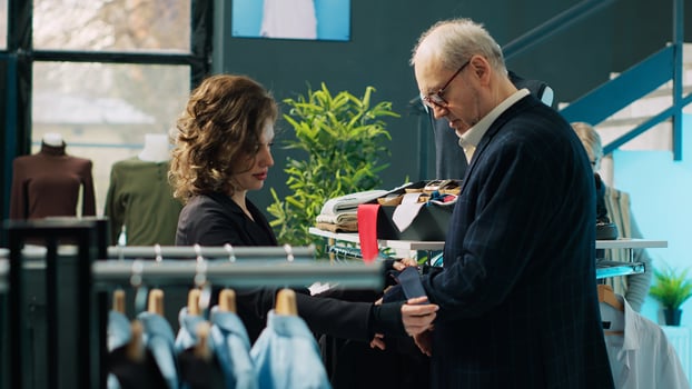 Woman employee presenting formal accessories to regular client, assisting him in choosing the right tie color to match his suit jacket. Store clerk helping customer, commercial activity. Camera A. photo