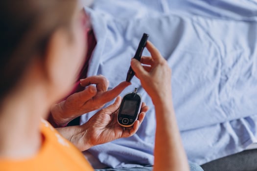 A female nurse checks an elderly man's blood sugar levels while sitting next to him and poking his finger with a needle. photo