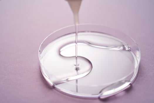 Serum or cosmetic oil flows into a transparent bowl on a purple background. photo