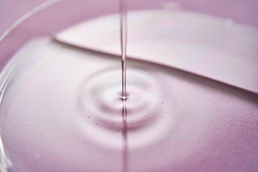 Serum or cosmetic oil flows into a transparent bowl on a purple background. photo