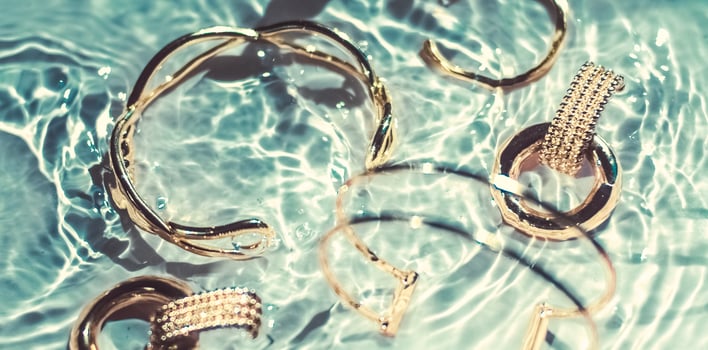 Golden bracelets, earrings, rings, jewelery on emerald water background, luxury glamour and holiday beauty design for jewelry brand ads photo