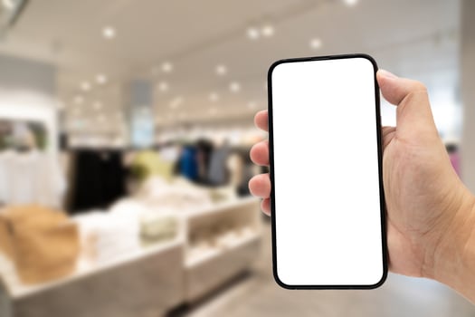 Hand holding blank screen smartphone for copy space on blurred clothing store. e-commerce app shopping mockup. social media, payment and shopping online concept. fashion and technology. photo