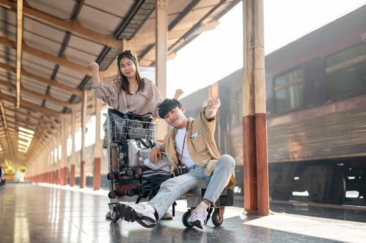 Cheerful couple are walking down the platform with a cart, commuting by a train at a railway station photo