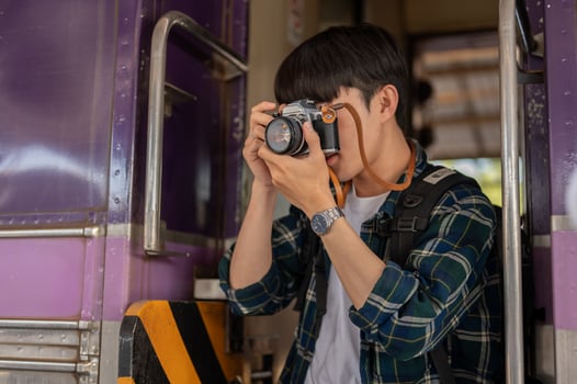 An Asian man traveler backpacker is taking pictures with his camera while getting off the train. photo