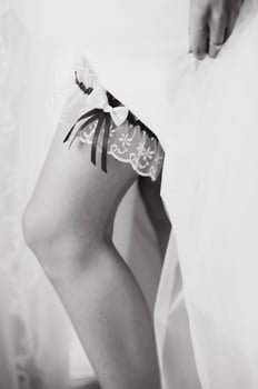 bride dresses garter on the leg. Picture of beautiful female barefoot legs in wedding dress. Bride dresses stockings on feet. Bride putting a wedding garter on her leg photo