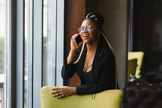 smiling black woman talking on the phone while resting in a cafeteria, selective focus photo