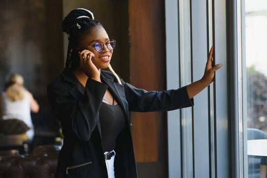 Smiling dark skinned woman in trendy wear laving cafe talking on mobile phone via roaming tariffs,african american millennial female walking and making smartphone call satisfied with connection photo