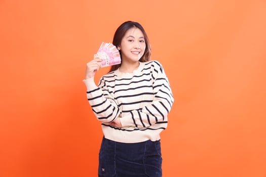 The expression of a cheerful Asian woman standing while holding a number of rupiah bills in her arms. for fashion, business and finance concept photo