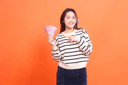 The expression of a cheerful Asian woman standing while holding some rupiah money for shopping. for fashion, business and finance concept photo