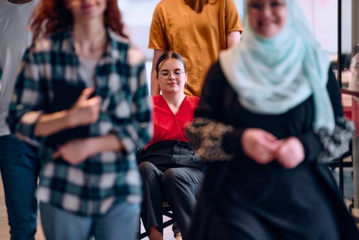 A diverse group of young business people walking a corridor in the glass-enclosed office of a modern startup, including a person in a wheelchair and a woman wearing a hijab photo