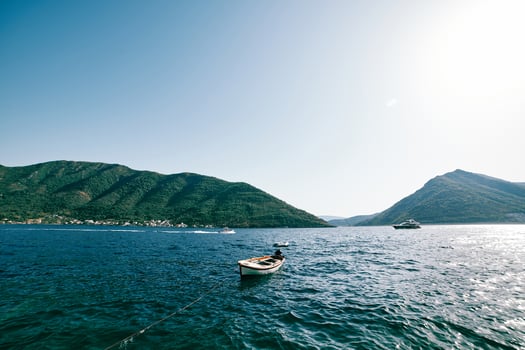 White fishing boat on a rope stands moored in the sea against a mountain ridge photo