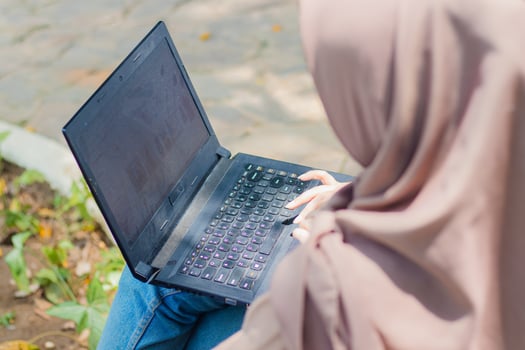 Two Asian girl focused on laptops discussing and checking together holding pens, laptops, books and clipboards while embracing in the campus park. students for education and lifestyle concepts photo