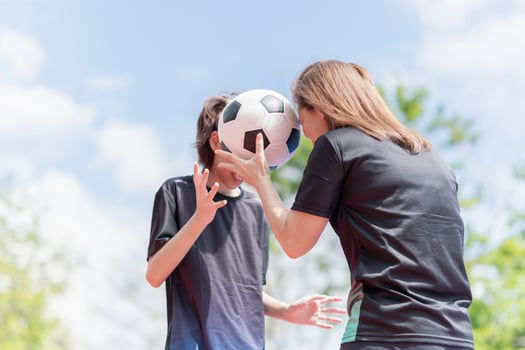 Happy mother and daughter are holding a ball on their heads together. Mom with child playing football outside on field photo